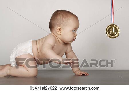 Stock Image - mixed race baby crawling towards gold medal. Fotosearch