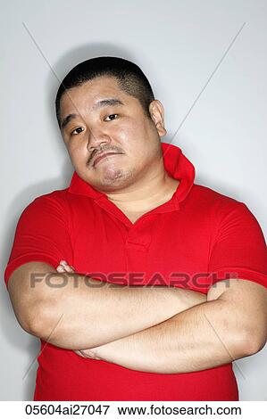 Stock Photo - Over weight Chinese man wearing red shirt frowning with arms folded.. Fotosearch