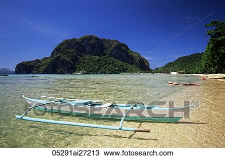 Stock Image - Philippines, Palawan, Bascuit Bay, El Nido, Outrigger on Tropical Beach at Sunset. Fotosearch