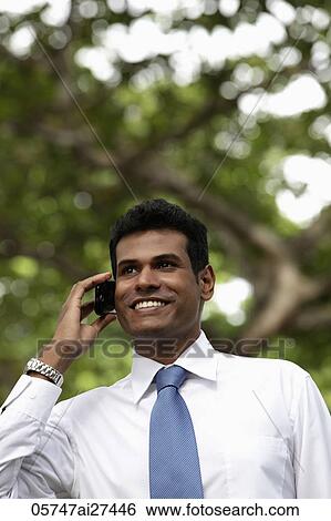 Stock Photograph - Portrait of Indian man talking on phone and smiling outdoors. Fotosearch