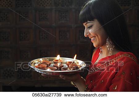 Stock Photo - Profile shot of Indian woman holding a tray of lit oil lamps. Fotosearch