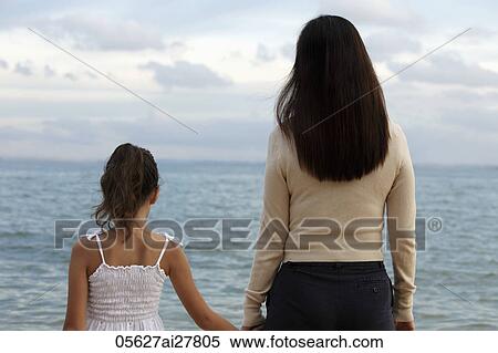 Rear view of mother and daughter holding hands looking at the water View Large Photo Image Stock Photography - Rear view of mother and daughter holding hands looking at the water. Fotosearch