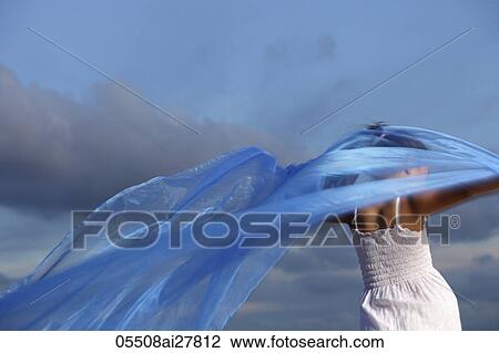 Stock Image - rear view of young girl holding blue cloth blowing in the wind. Fotosearch