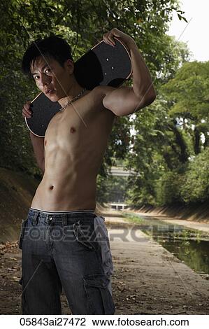 Stock Image - Shirtless Chinese man holding skate board outside. Fotosearch