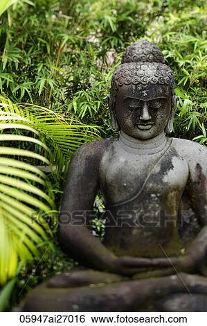 Stock Photograph - stone buddha surrounded by trees. Fotosearch
