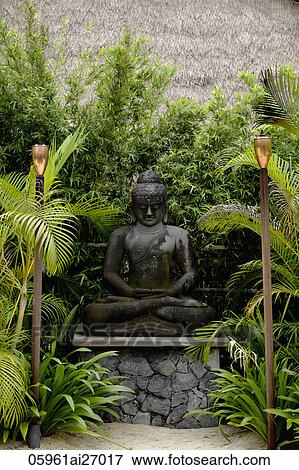 Stock Photo - stone buddha surrounded by trees with torches in foreground. Fotosearch