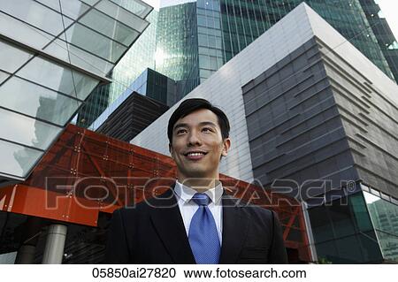 Stock Image - Young businessman smiling in front of modern buildings. Fotosearch