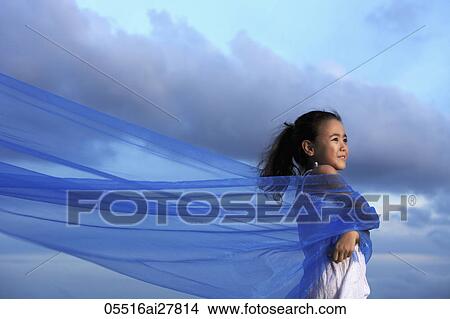 Picture - Young girl holding blue cloth blowing in the wind with blue sky background. Fotosearch
