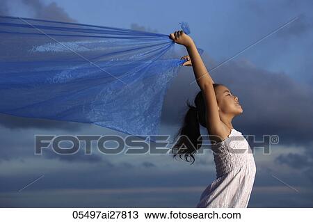Stock Image - young girl holding up blue cloth, blue sky background. Fotosearch