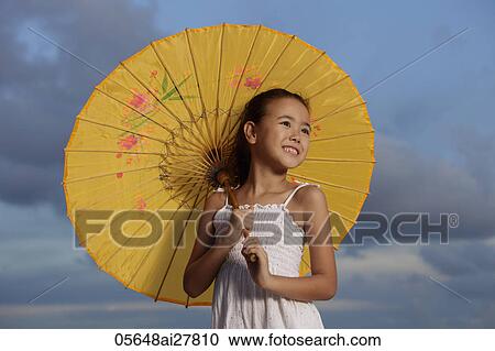Stock Image - young girl smiling holding yellow Chinese umbrella, blue sky background. Fotosearch