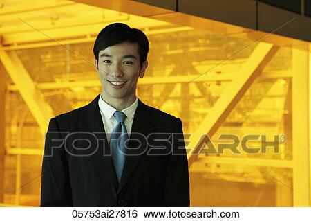 Stock Photograph - Young man smiling and wearing a business suit standing in front of orange tinted glass. Fotosearch