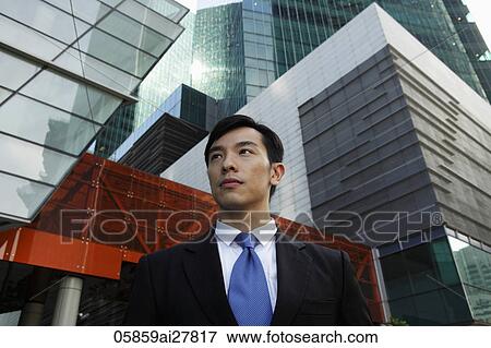 Stock Photo - Young man wearing a suit standing in front of modern buildings. Fotosearch