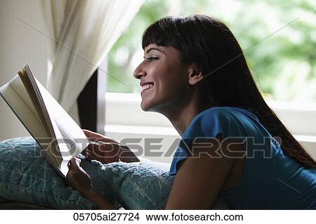 Young woman laying on stomach reading a book and smiling View Large Photo Image Picture - Young woman laying on stomach reading a book and smiling. Fotosearch