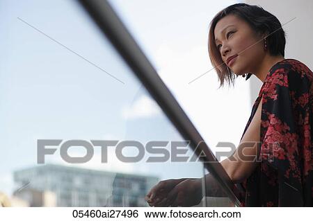 Stock Photograph - Young woman looking over balcony. Fotosearch