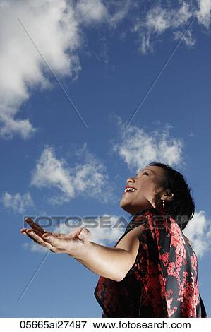 Young woman looking up at sky with arms outstretched View Large Photo Image Stock Photo - Young woman looking up at sky with arms outstretched. Fotosearch