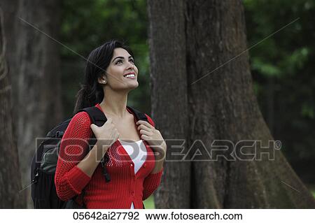 Young woman wearing a back pack looking up at trees and smiling View Large Photo Image Stock Image - Young woman wearing a back pack looking up at trees and smiling. Fotosearch
