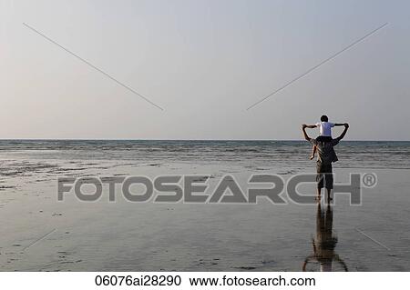 Stock Image - Boy sitting on father's shoulders and holding hands and looking at the ocean. Fotosearch