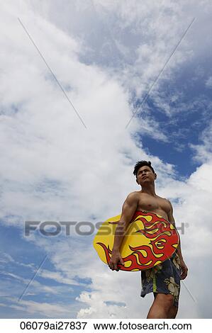 Stock Photo - Chinese man holding skim board blue sky and clouds background. Fotosearch