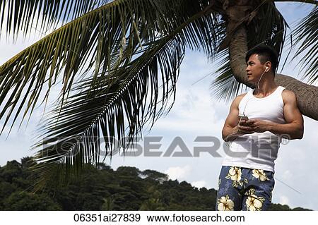 Chinese man leaning against palm tree listening to music View Large Photo Image Stock Photo - Chinese man leaning against palm tree listening to music. Fotosearch