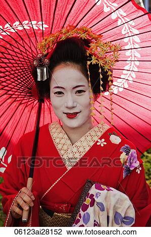 Stock Image - Head shot of Geisha wearing red Kimono and holding red umbrella. Fotosearch