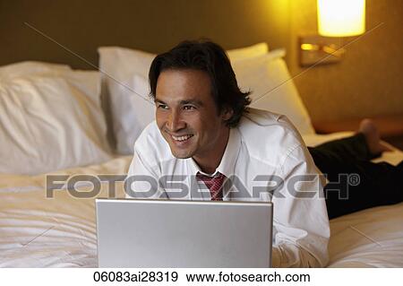 man lying on bed smiling while working on lap top View Large Photo Image Stock Photo - man lying on bed smiling while working on lap top. Fotosearch
