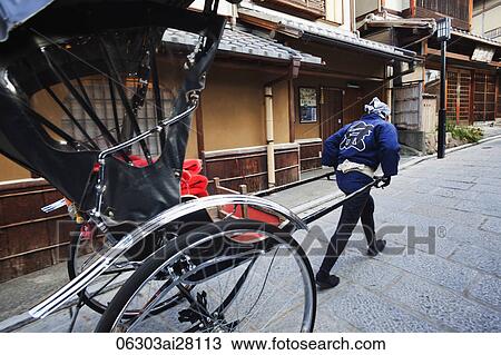 Stock Image - man pulling rickshaw in front of houses. Japan, Kyoto. Fotosearch