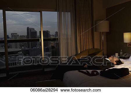 man wearing suit and laying down on bed in hotel room in the evening. View Large Photo Image Picture - man wearing suit and laying down on bed in hotel room in the evening.. Fotosearch