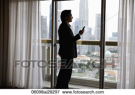 Man wearing suit holding phone looking out window View Large Photo Image Stock Photo - Man wearing suit holding phone looking out window. Fotosearch