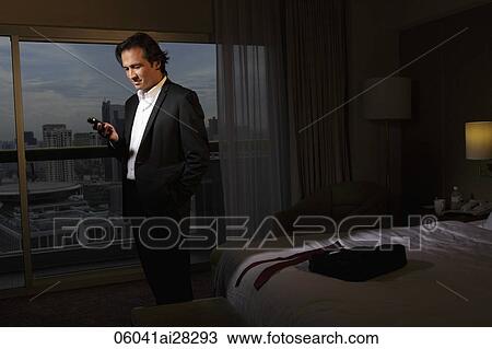 Stock Image - man wearing suit in hotel room looking at phone. Fotosearch