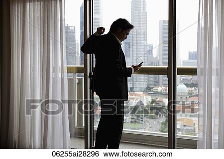 Man wearing suit, looking at phone near window View Large Photo Image Stock Photograph - Man wearing suit, looking at phone near window. Fotosearch