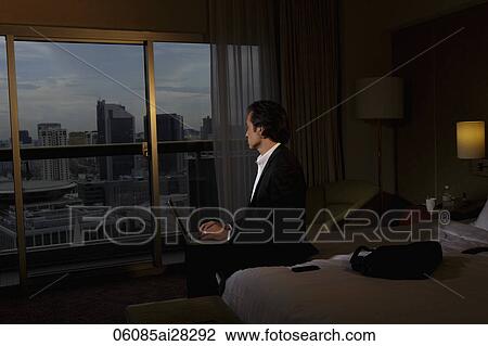 Man working on lap top in hotel room looking out the window in the evening. View Large Photo Image Stock Image - Man working on lap top in hotel room looking out the window in the evening.. Fotosearch