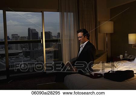 Stock Photography - Man working on lap top sitting in hotel room in the evening. Fotosearch
