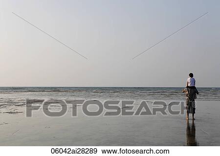 Stock Photo - Son sitting on father's shoulders looking at beach. Fotosearch