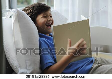 Young boy looking at book and laughing View Large Photo Image Stock Photography - Young boy looking at book and laughing. Fotosearch