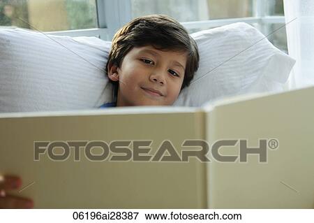 Young boy reading book by window and smiling View Large Photo Image Stock Photo - Young boy reading book by window and smiling. Fotosearch