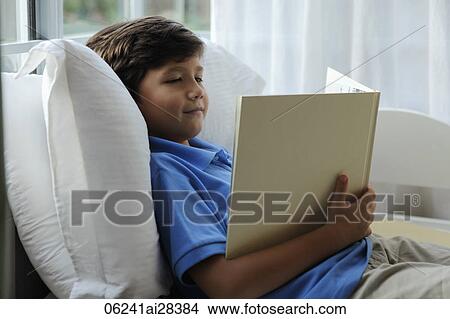 Picture - young boy sitting in bed reading book. Fotosearch