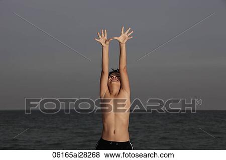 Young boy standing in front of ocean looking up with hands outstretched View Large Photo Image Stock Photo - Young boy standing in front of ocean looking up with hands outstretched. Fotosearch