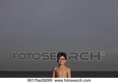Young boy standing in front of ocean smiling with goggles on his head View Large Photo Image Stock Photo - Young boy standing in front of ocean smiling with goggles on his head. Fotosearch
