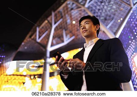 Young man in suit using phone in front of building at night View Large Photo Image Stock Photo - Young man in suit using phone in front of building at night. Fotosearch