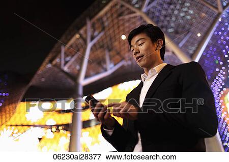 Stock Photo - Young man in suit using phone in front of building at night. Fotosearch