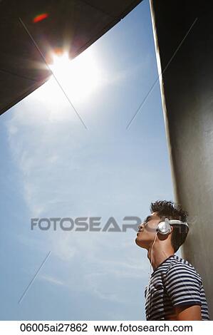 Young man leaning against wall wearing headphones View Large Photo Image Stock Image - Young man leaning against wall wearing headphones. Fotosearch