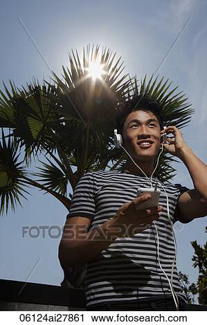 Stock Image - Young man listening to music outside on a sunny day. Fotosearch