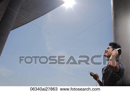Young man listening to music outside on a sunny day View Large Photo Image Stock Image - Young man listening to music outside on a sunny day. Fotosearch