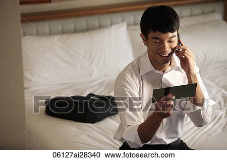 Stock Image - Young man looking at ticket and talking on phone smiling. Fotosearch