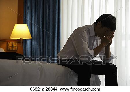Young man sitting on bed with head in hands in the evening View Large Photo Image Picture - Young man sitting on bed with head in hands in the evening. Fotosearch