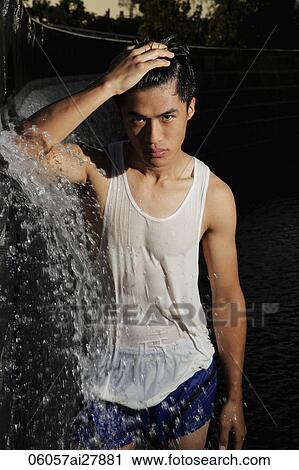 Stock Image - Young man standing in water fountain. Fotosearch