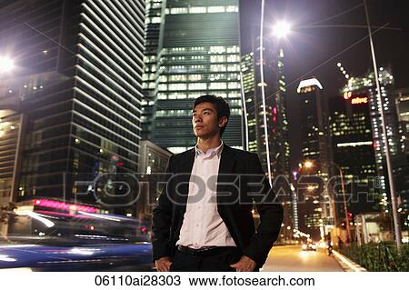 Young man standing on street at night with buildings in background View Large Photo Image Stock Image - Young man standing on street at night with buildings in background. Fotosearch