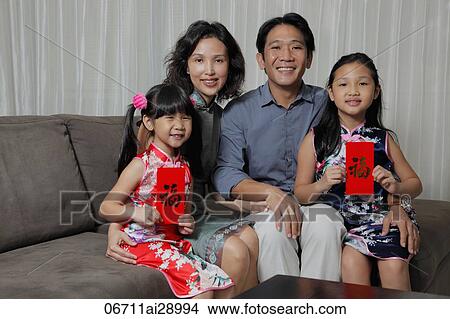Picture - Chinese family sitting together with daughters holding red envelopes (Hong Bao). Fotosearch