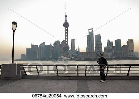 Picture - Chinese man standing on boardwalk with Shanghai skyline in background. Fotosearch