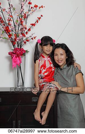 Stock Photo - Chinese mother and daughter wearing Cheongsams sitting near flowers. Fotosearch